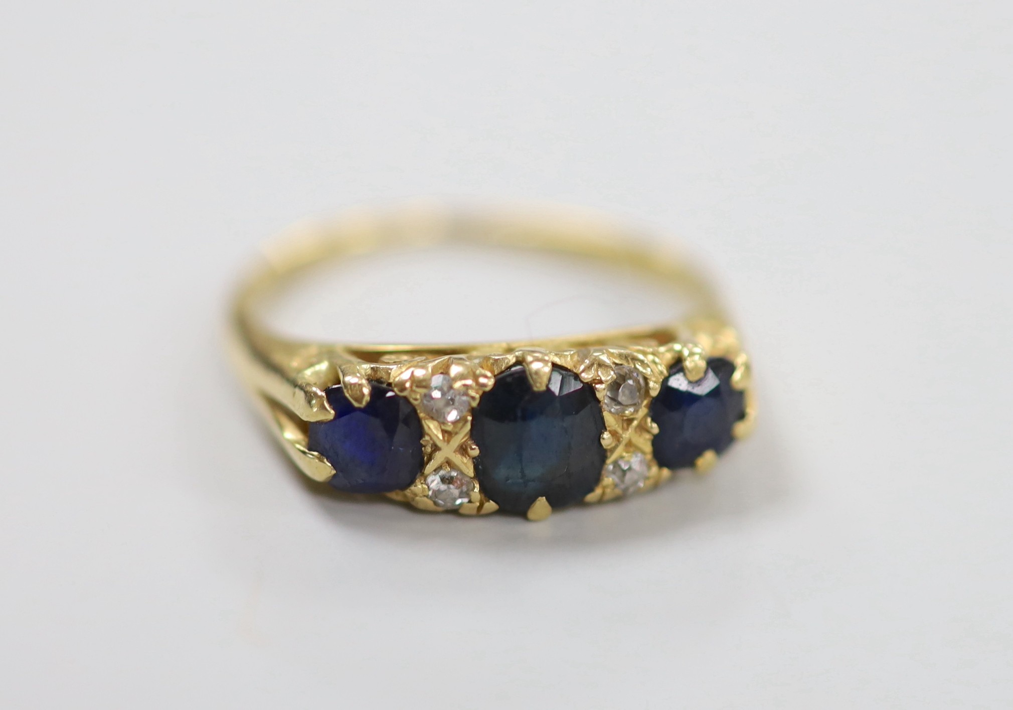 An early to mid 20th century gold, three stone sapphire and four stone diamond chip set half hoop ring, size O, gross weight 4.5 grams.